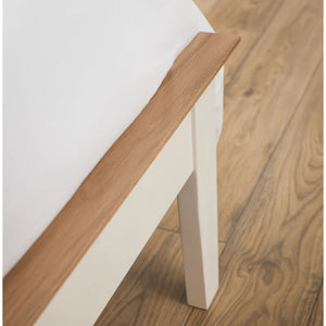 Close-up of a wooden and white bed frame on a wooden floor.