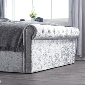 Gray upholstered bed with textured finish in a room with large windows and curtains.