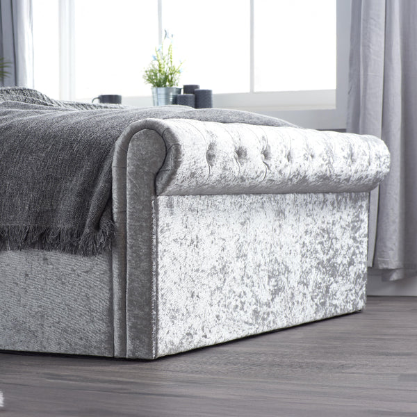 Gray upholstered bed with textured finish in a room with large windows and curtains.