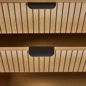 Close-up of a wooden drawer with slatted design and black handles.