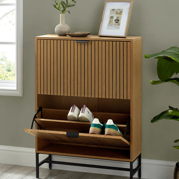 Wooden shoe cabinet with open door showing shoes, placed against a wall with a plant and framed picture.