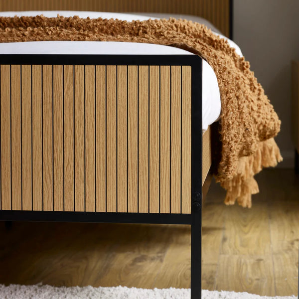 Wooden bed frame with a textured brown blanket on a wooden floor.