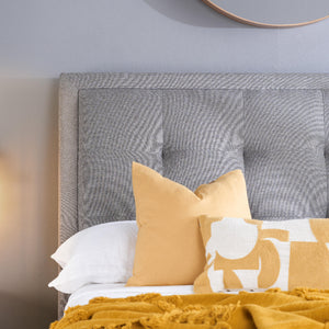Gray upholstered headboard with yellow and white pillows on a bed.