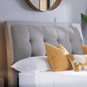 Gray upholstered headboard with white and yellow pillows on a bed.
