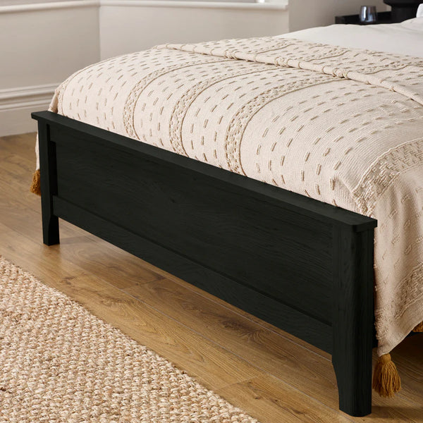 Black bed frame with beige bedding on a wooden floor
