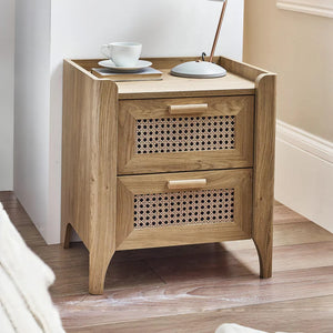 Wooden side table with two drawers and a cup on top in a room setting.