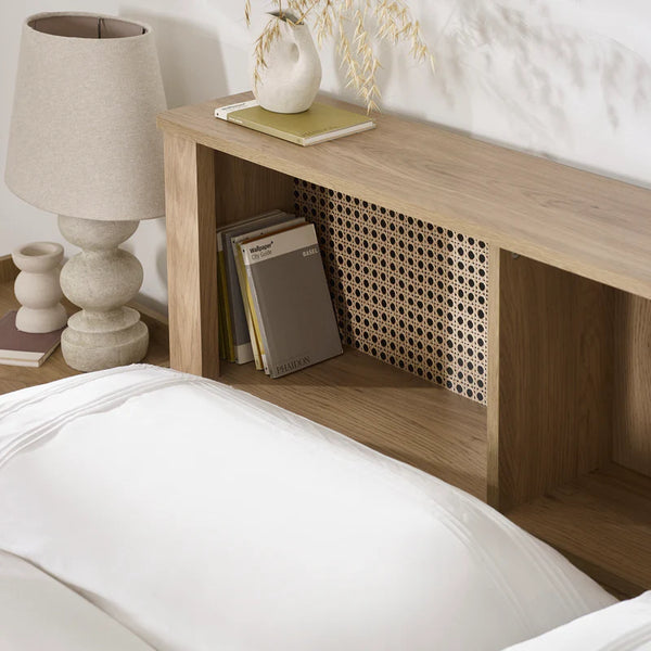 Wooden nightstand with books and a lamp next to a bed