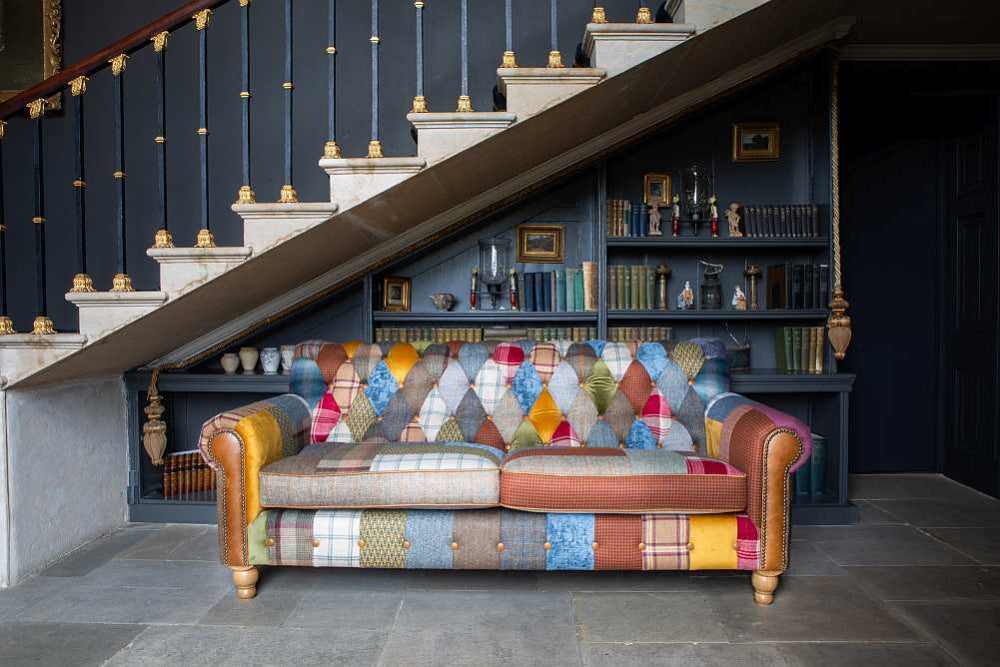 Multicolored patchwork sofa under a staircase with a bookshelf in the background.