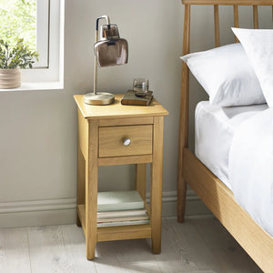 Wooden bedside table with lamp and glasses next to a bed in a bedroom.