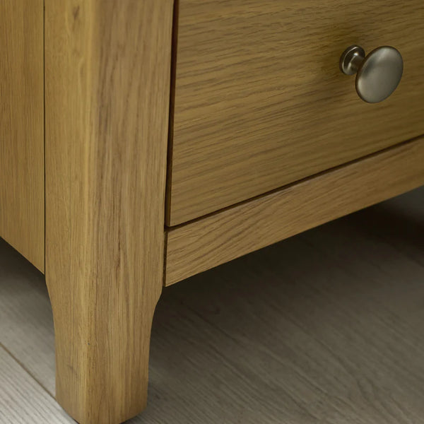Close-up of a wooden drawer with a metal handle on a light wood floor.