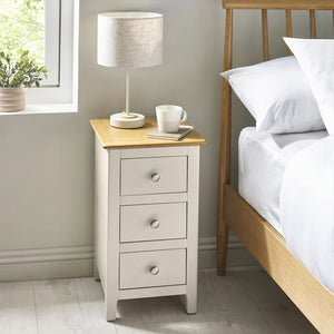 Nighstand with three drawers next to a bed in a bedroom setting.