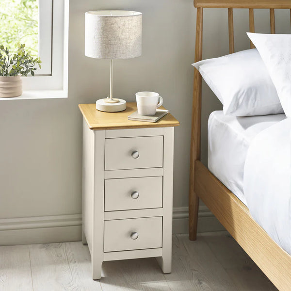 Nighstand with three drawers next to a bed in a bedroom setting.
