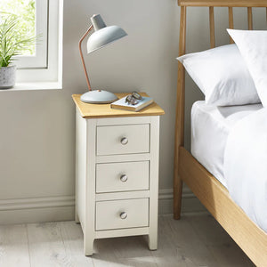 White nightstand with three drawers next to a bed in a bedroom setting.