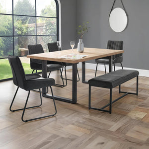Dining area with wooden table, black chairs, and bench in a room with large windows.