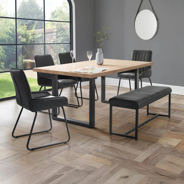 Dining area with wooden table, black chairs, and bench in a room with large windows.