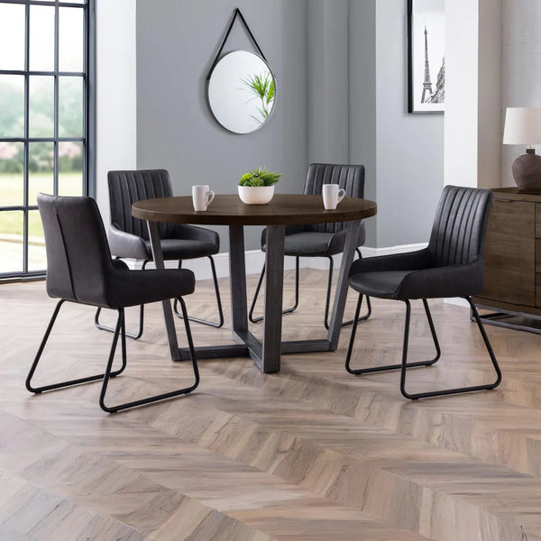 Dining room with a round wooden table and black chairs on a herringbone wood floor.