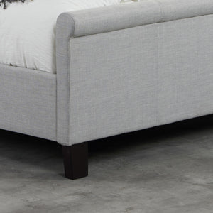 Gray upholstered bed frame with dark wooden legs on a concrete floor.