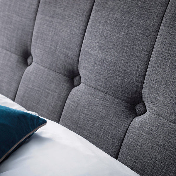 Gray upholstered headboard with tufted design on a bed.