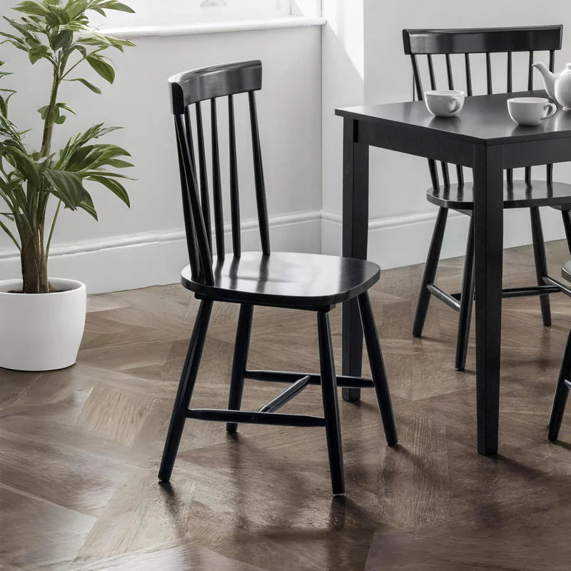 Four black dining chairs with slatted backrests on a white background