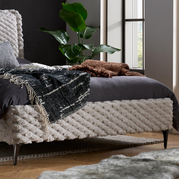 Cozy bedroom with textured bed, cushions, and a plant
