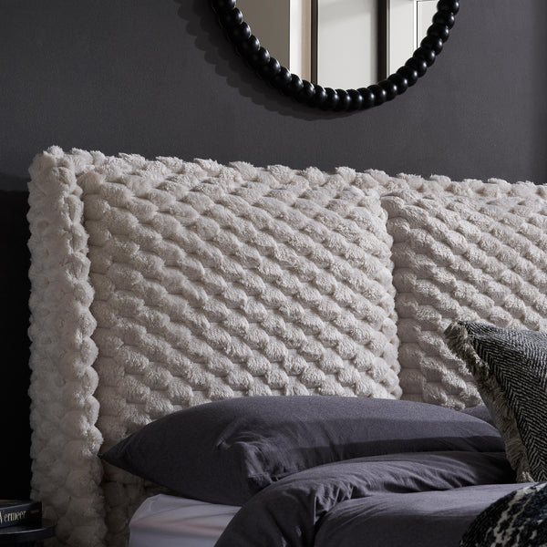 Textured white headboard with dark pillows against a dark wall.