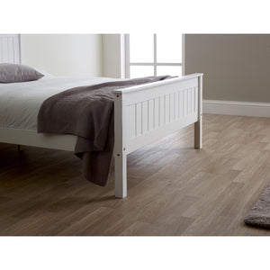 White wooden bed with a brown blanket on a wooden floor.