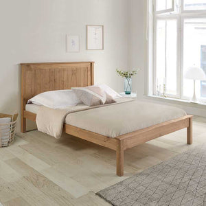Wooden bed in a bright bedroom with large windows and minimal decor.