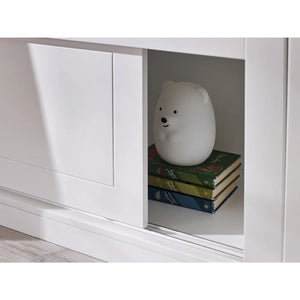 White bear-shaped night light on books inside a white cabinet.