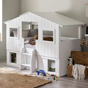 White children's playhouse bed with toys and a rug on the floor
