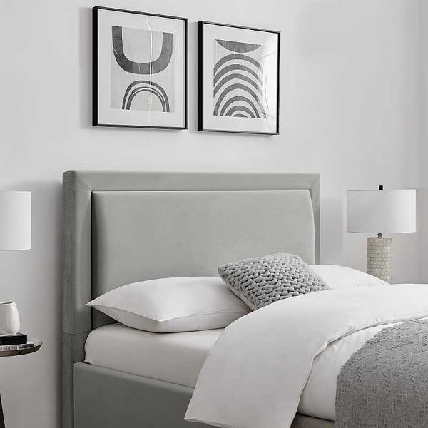 Gray upholstered bed with white bedding and abstract art on a white wall