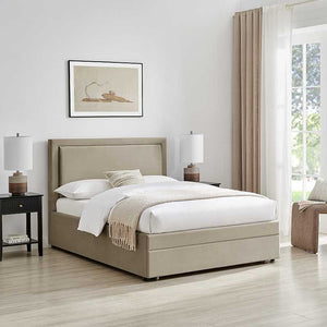 Beige upholstered bed in a bright bedroom with white walls and large windows.