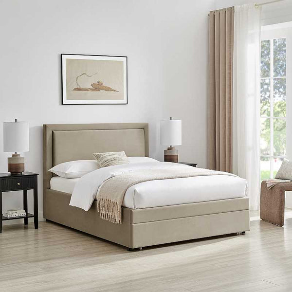 Beige upholstered bed in a bright bedroom with white walls and large windows.
