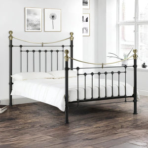 Black metal bed with gold accents in a room with white walls and wooden flooring.