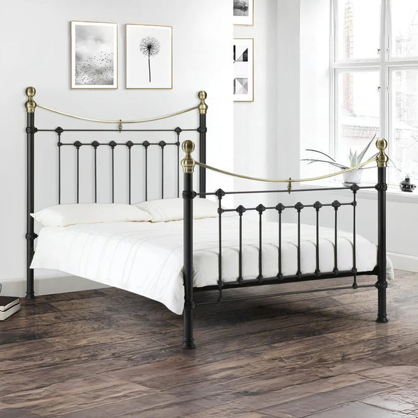 Black metal bed with gold accents in a room with white walls and wooden flooring.