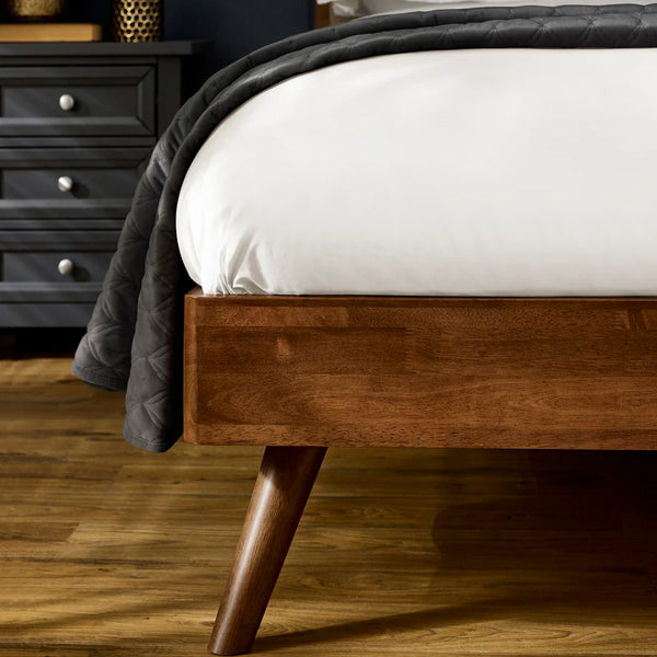 Wooden bed frame with a gray blanket on a wooden floor