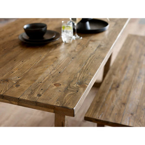 Wooden dining table with a rustic finish, set with black dishes and a glass.