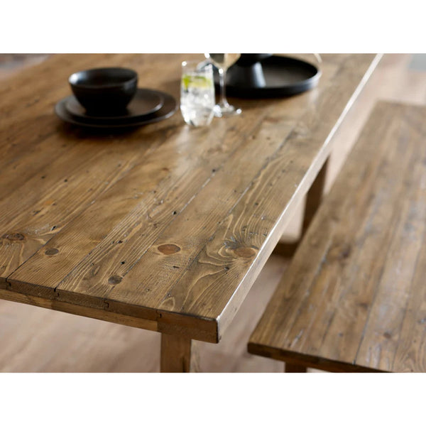 Wooden dining table with a rustic finish, set with black dishes and a glass.