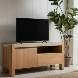 Wooden TV stand with a television on it, placed against a light-colored wall with plants in the background.