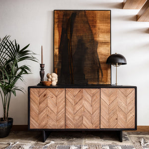 Wooden sideboard with chevron pattern in a room with a staircase and plant.