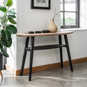 Wooden table with black legs against a white wall with a framed picture and a plant.