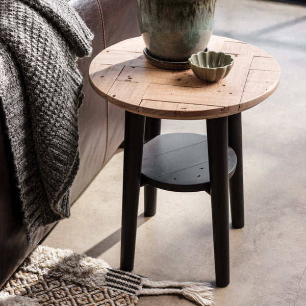 Round wooden side table with a plant and small bowl next to a sofa.