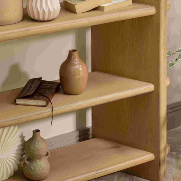 Wooden book shelf with decorative vases and a book against a neutral wall.