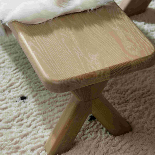 Wooden stool with a fur-covered seat on a carpeted floor