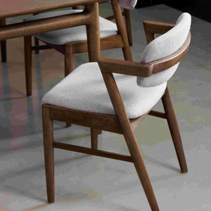 Dining chair with wooden frame and white cushion in a room setting.