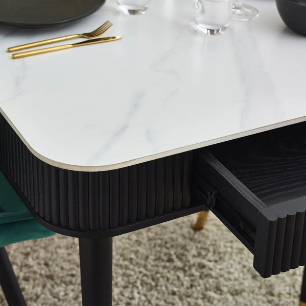 Black dining table with white marble top and gold cutlery on a carpeted floor.