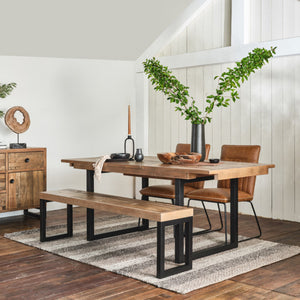Dining room with wooden table, chairs, and bench on a rug, against a white wall.