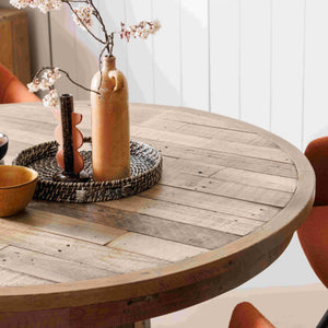 Round wooden table with decorative items in a room with orange chairs.